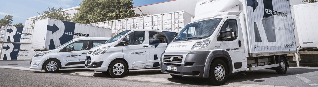 Drei weiße GEBR. ROORDINK-Fahrzeuge stehen vor Containern und einem Gebäude auf einem Firmengelände.